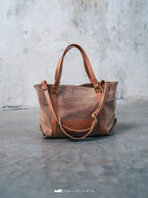 Kép betöltése a galériamegjelenítőbe: Geantă maro din piele pe o suprafață gri, cu perete de beton pe fundal.
