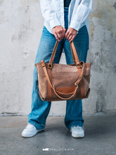 Încărcați imaginea în vizualizatorul Galeriei, Persoană care ține o geantă maro din piele, pe fundal cu perete de beton.

